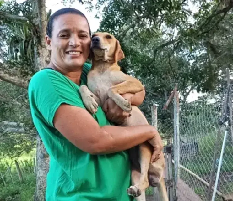 Voluntário agachado no canil, com dois cães no colo e outros ao redor das casinhas de concreto